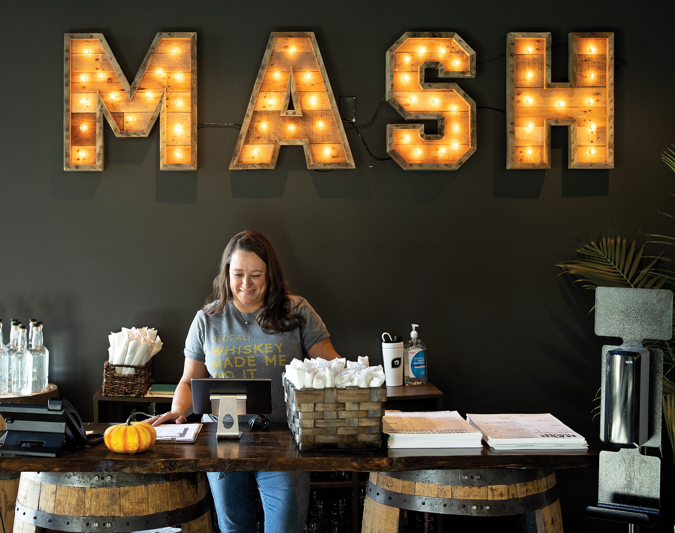 a restaurant employee in front of a wall with an illuminated MASH sign