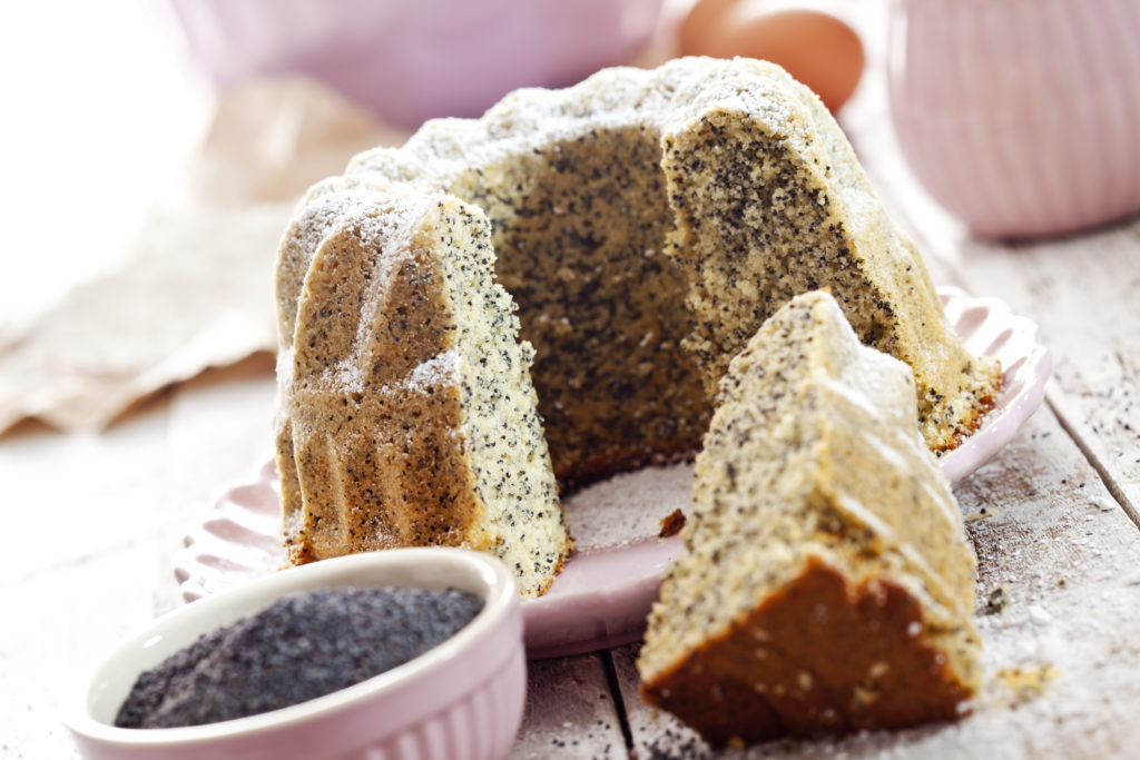 poppyseed cake recipe image showing a cut cake on a pink plate with poppyseeds in a bowl