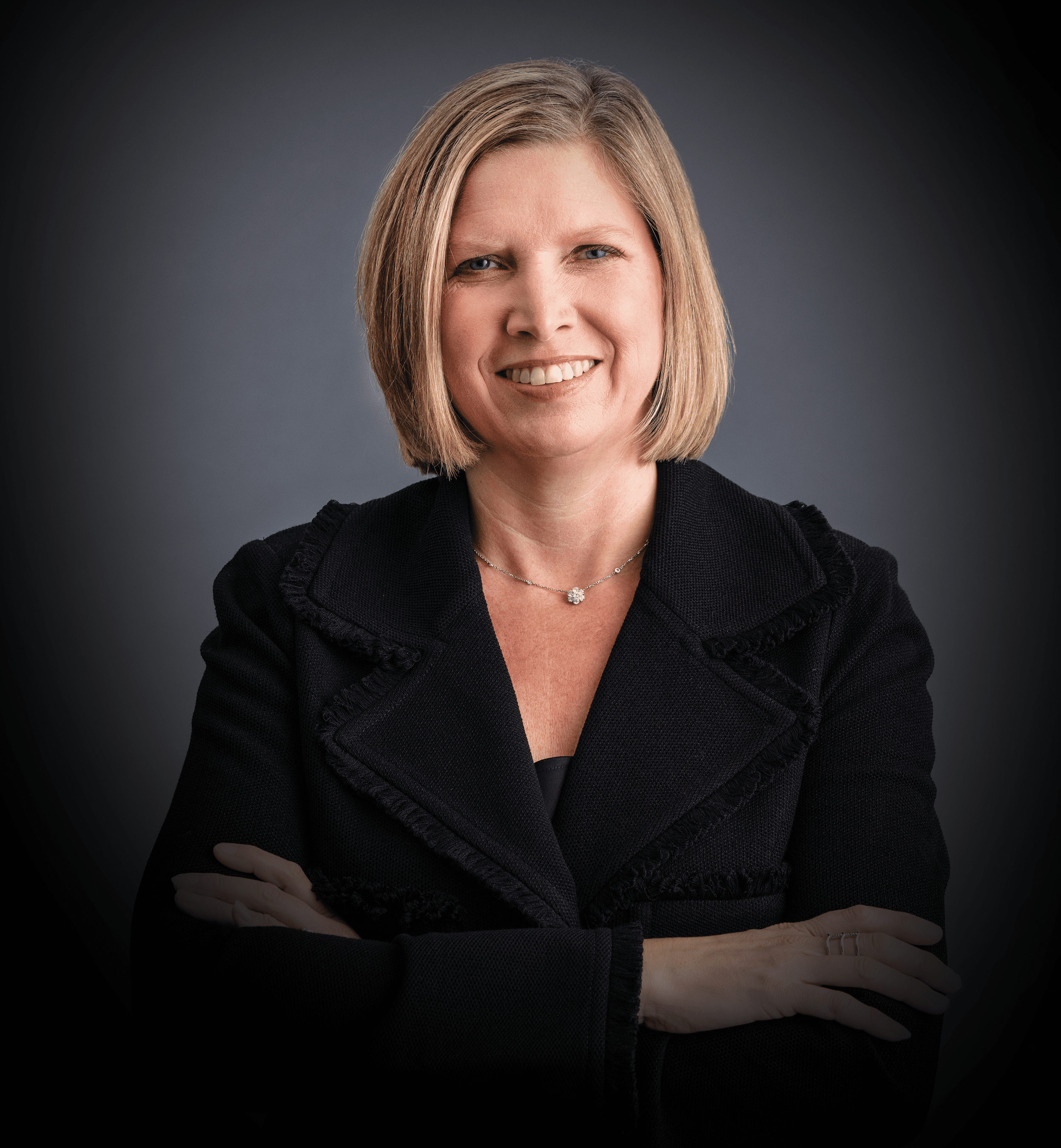 Jennifer Rumsey, Cummins CEO sports a blonde bob and a black jacket in this photo studio image with a grey background