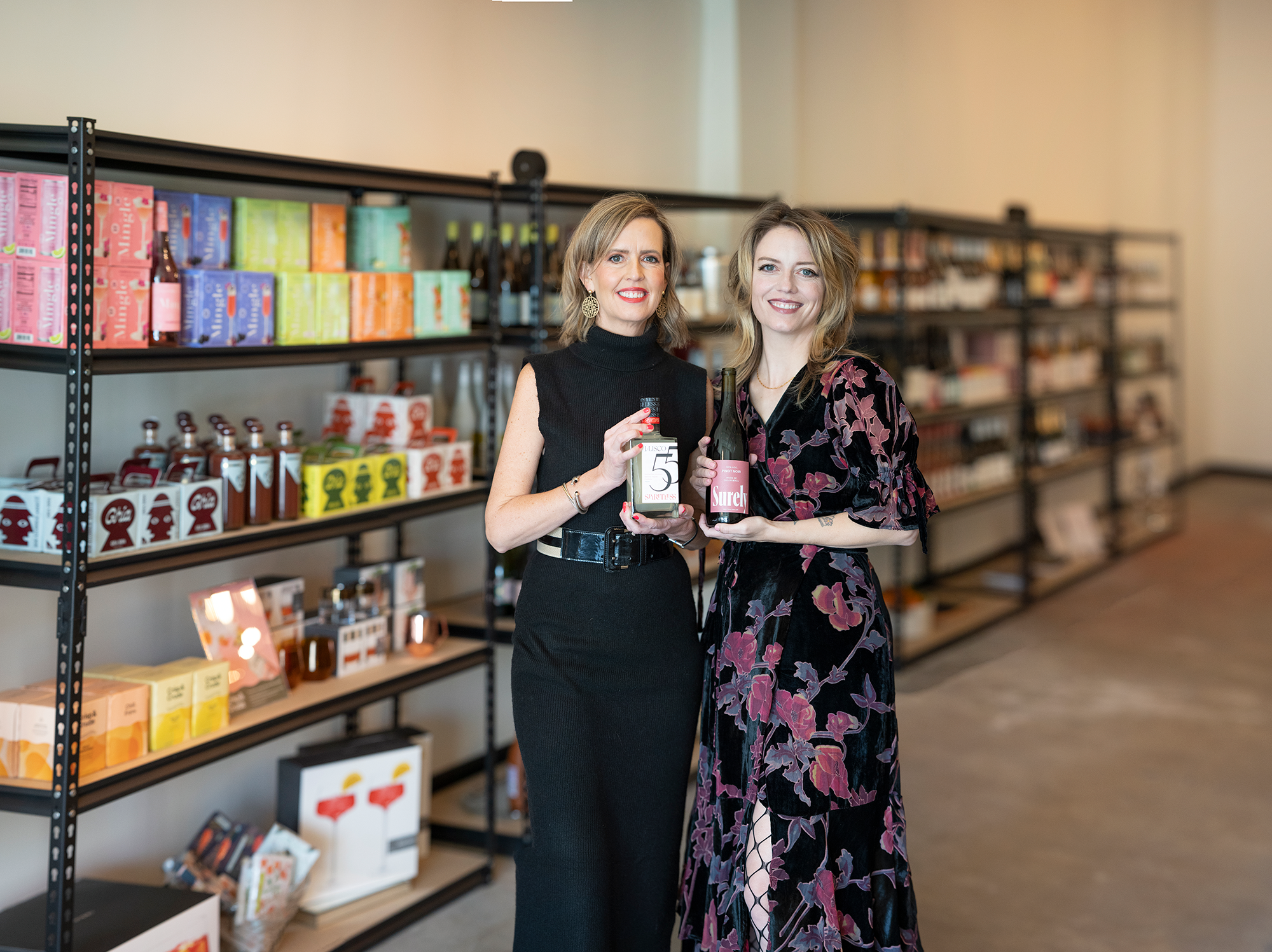 Loren's AF owners and sister pose in front of shelves of nonalcoholic beverages like the bottles they hold